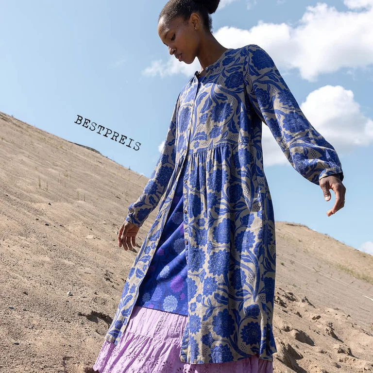 Eine Frau in einem geblümten blauen Hemdblusenkleid von Gudrun Sjödén.