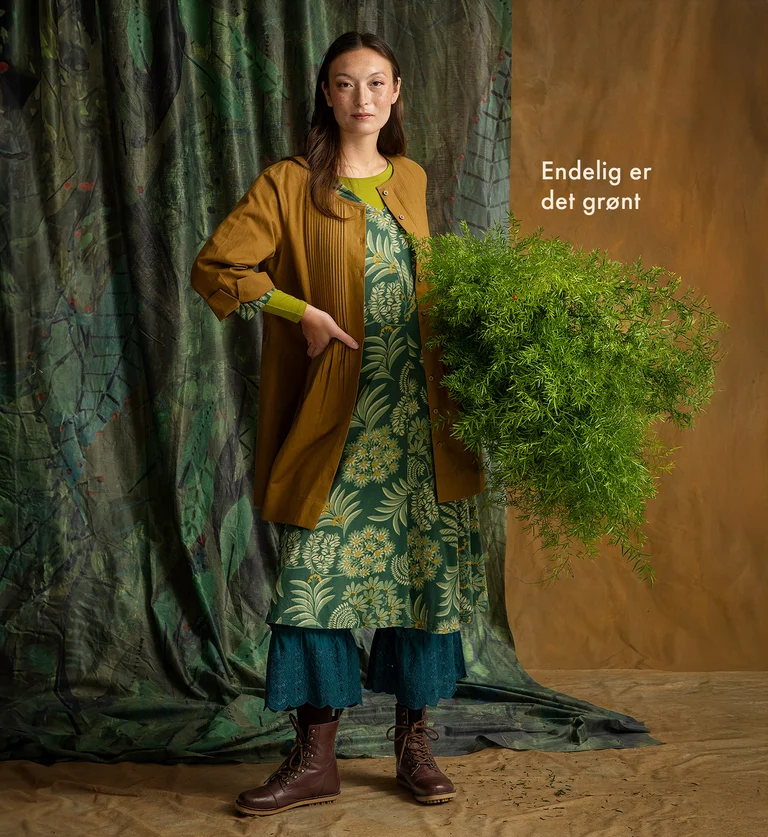 A woman holding a green plant, wearing layers of garments from Gudrun Sjödén.