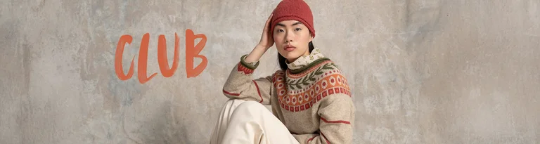 Une femme portant un pull en maille à motifs et un bonnet rouge se tient devant un fond neutre avec le texte « CLUB » en rouge.