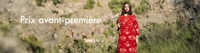 Une femme tenant une brindille verte devant son visage et portant une robe portefeuille rouge signée Gudrun Sjödén.