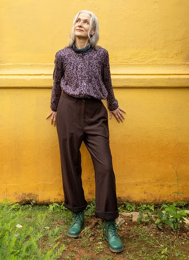 A woman wearing a purple blouse and brown trousers from Gudrun Sjödén.