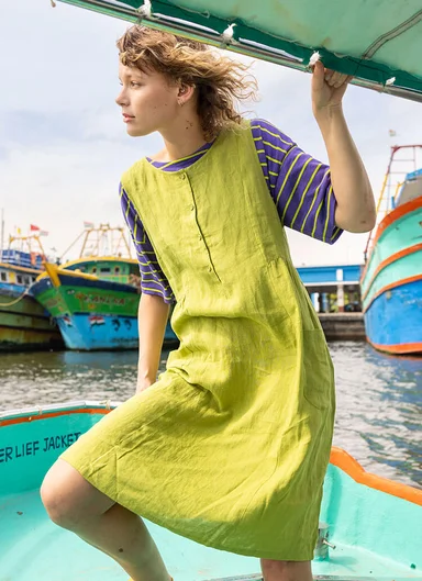 A woman wearing a green, woven dress over a striped T-shirt from Gudrun Sjödén.