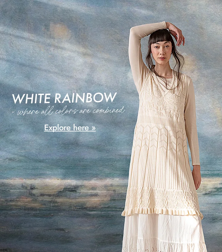 A woman wearing layers of white clothes from Gudrun Sjödén against a background that looks like an abstract oil painting in shades of blue-grey.