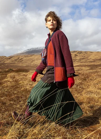 A woman walking in a windy mountain landscape wearing layers of clothes from Gudrun Sjödén.