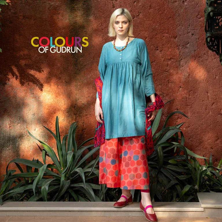 A woman wearing a woven blue dress and patterned trousers from Gudrun Sjödén.