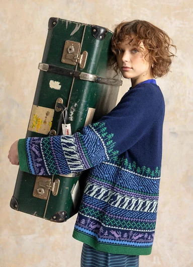 A woman hugging a suitcase wearing a patterned knitted sweater from Gudrun Sjödén.