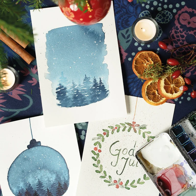 Aquarelkleuren en zelfgemaakte kerstkaarten geschilderd in blauw- en groentinten op een creatieve plek.