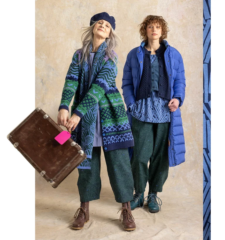 Deux femmes avec des valises à la main, portant des superpositions de vêtements signés Gudrun Sjödén.
