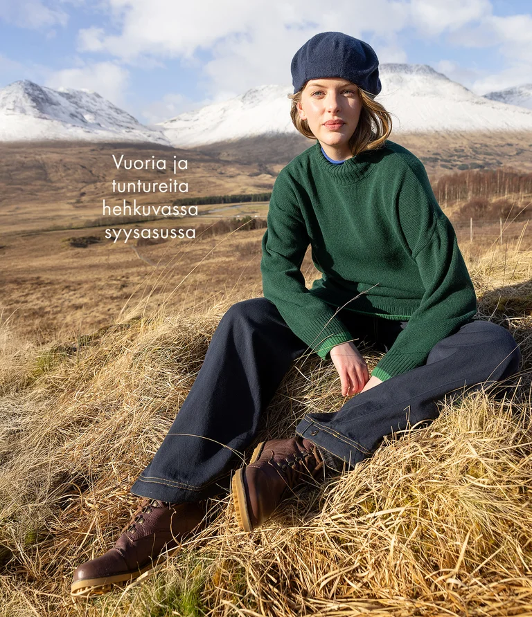 A woman sitting in a mountain setting wearing layers of clothing from Gudrun Sjödén. On her head, she is wearing a beret from Gudrun Sjödén.