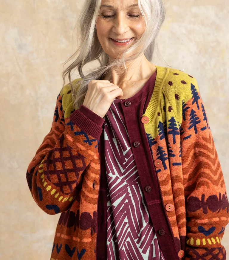 A closeup of a woman wearing layers of patterned clothing in shades of red and orange from Gudrun Sjödén.