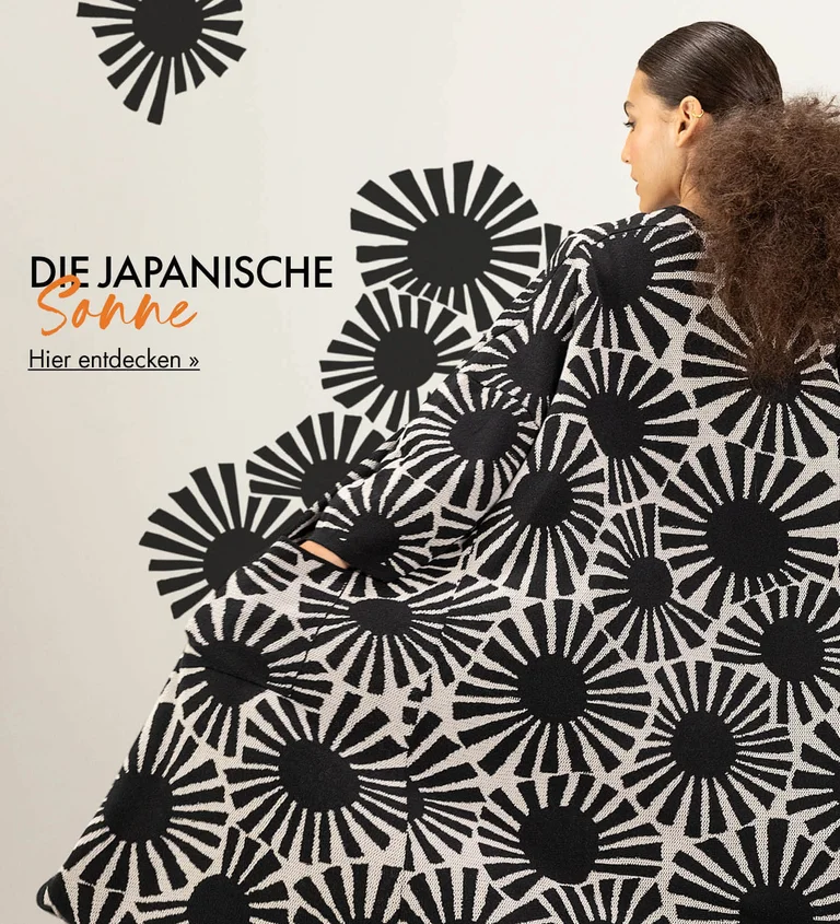 Eine Frau von hinten, in einer Langstrickjacke mit schwarzen grafischen Sonnen von Gudrun Sjödén. Sich von der Strickjacke ins Bild hinein ausbreitendes Muster.