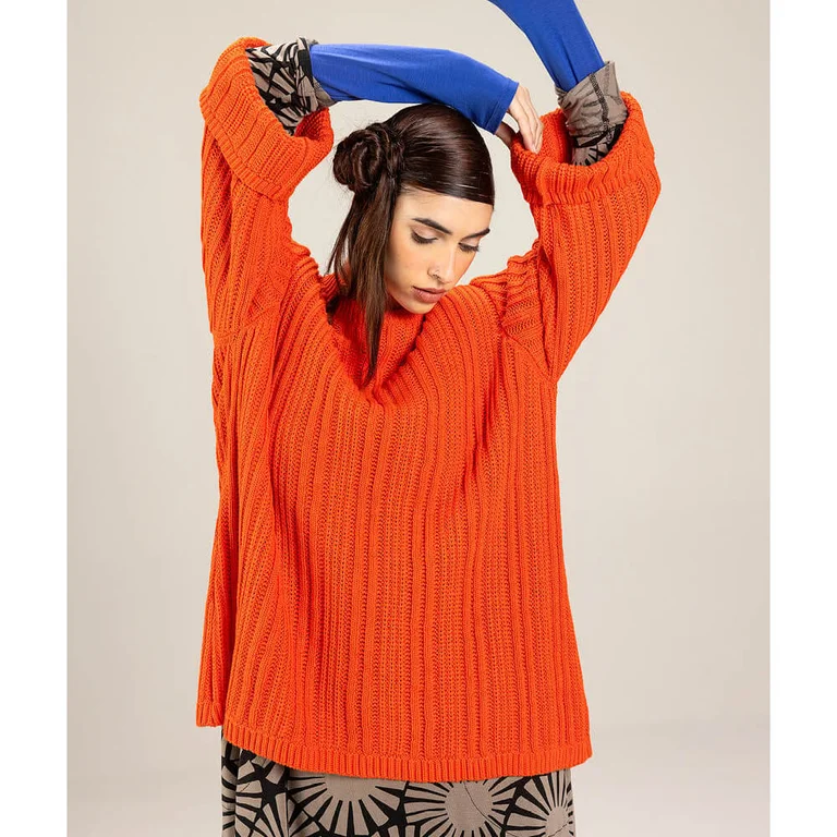 Eine Frau im leuchtend orangefarbenen Strickpullover von Gudrun Sjödén.