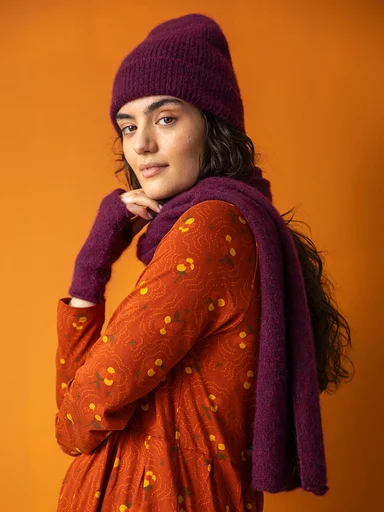 A woman wearing a reddish purple beanie and fingerless gloves from Gudrun Sjödén. 