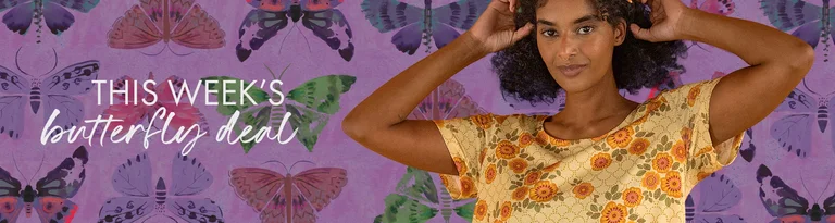 A woman in a patterned yellow dress stands in front of a purple wall with butterflies.