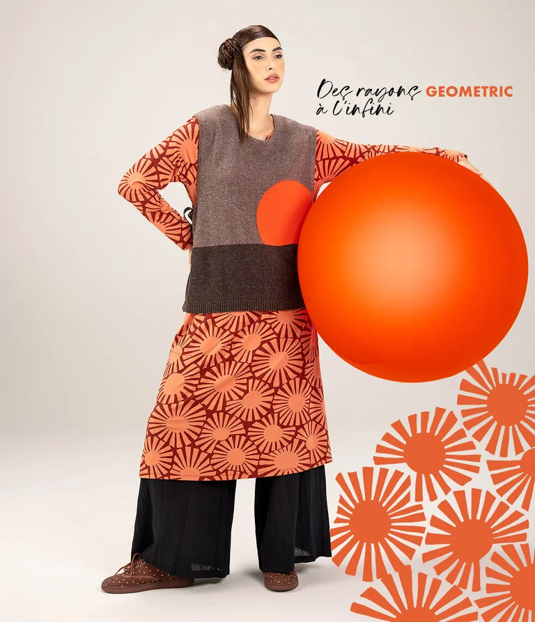 A woman standing with a large red ball, wearing layers of clothing from Gudrun Sjödén’s spring extra collection 2026.