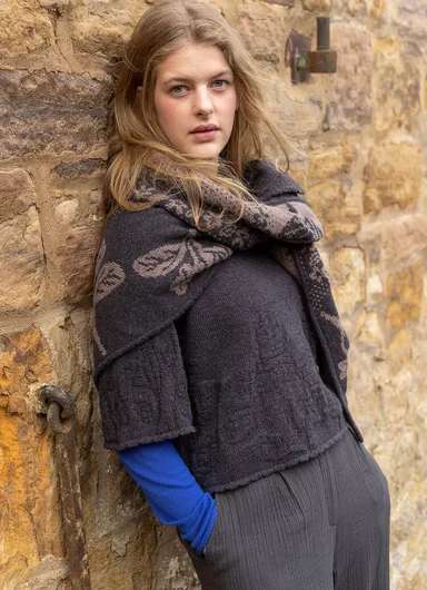 A woman leaning against a stone wall wearing clothes in earthy hues from Gudrun Sjödén.