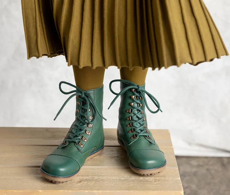 Des jambes portant une jupe plissée et des bottines vertes provenant de la collection d'hiver 2025 de Gudrun Sjödén.
