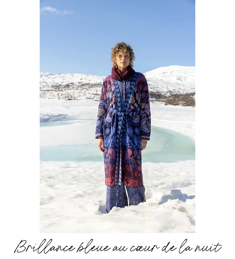 Une femme se tenant dans un paysage enneigé et portant des superpositions de vêtements provenant de la collection de Noël 2025 de Gudrun Sjödén. 