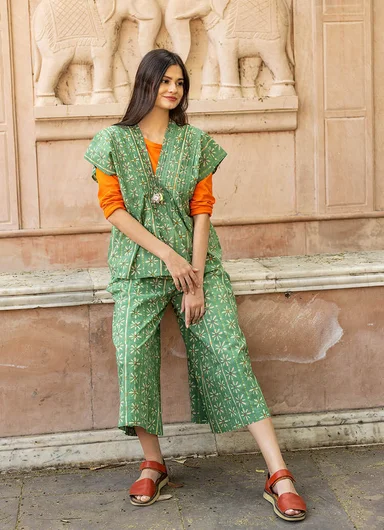 A woman wearing a matching patterned green top and trousers in woven fabric from Gudrun Sjödén.