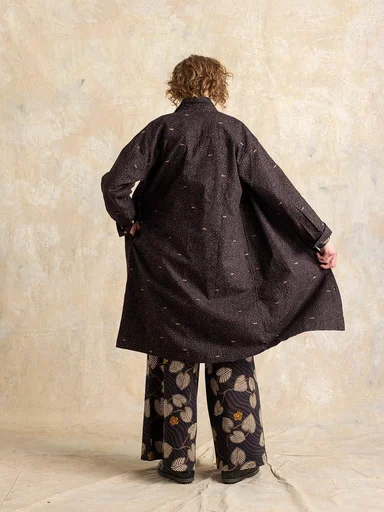 A woman with her back to the camera wearing a brown dress and patterned brown pants from Gudrun Sjödén.