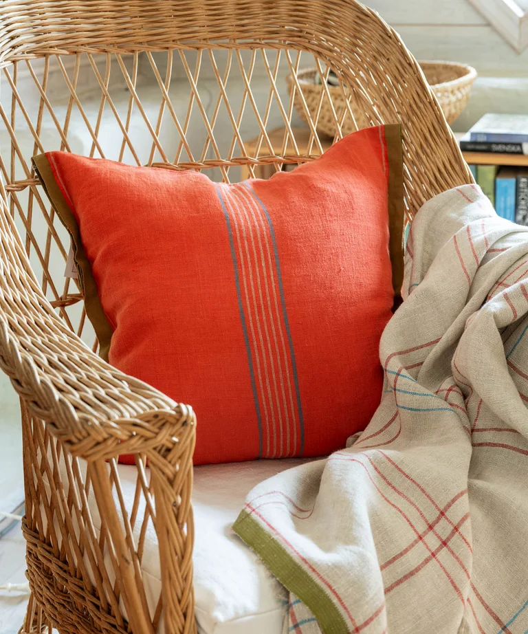 A cushion cover in a linen blend in the color chili from Gudrun Sjödén on a rattan chair.