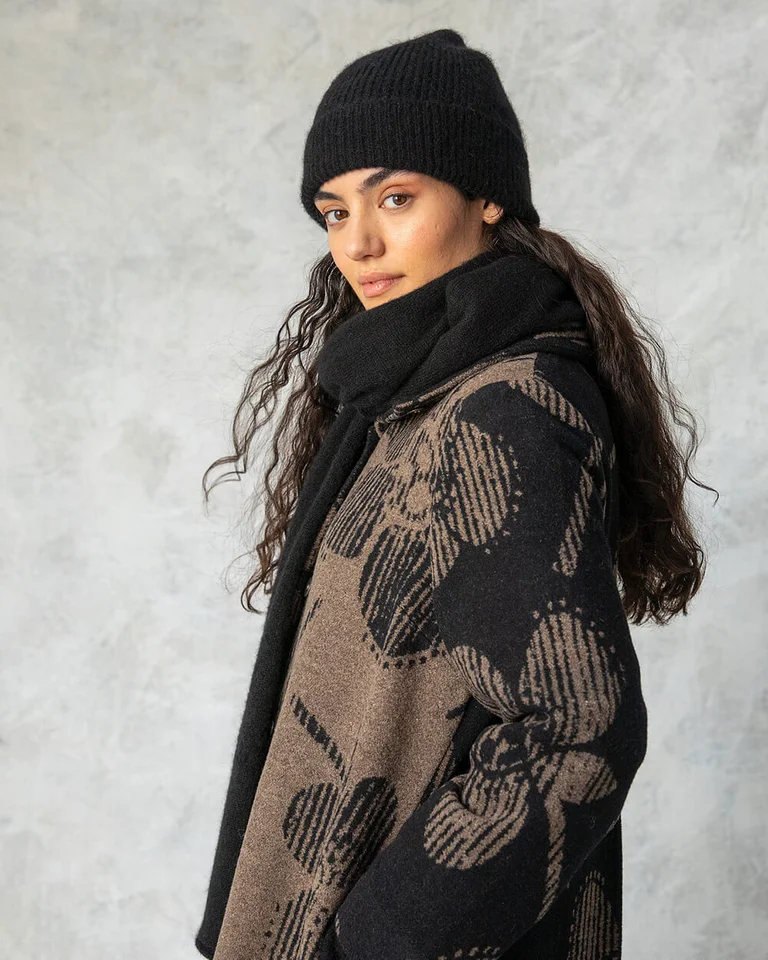 A woman wearing a patterned wool coat and knitted beanie from Gudrun Sjödén. 