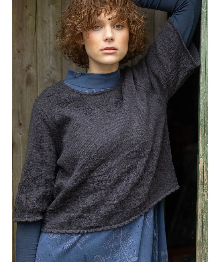 A closeup of a woman wearing a gray sweater over a blue patterned top from Gudrun Sjödén.