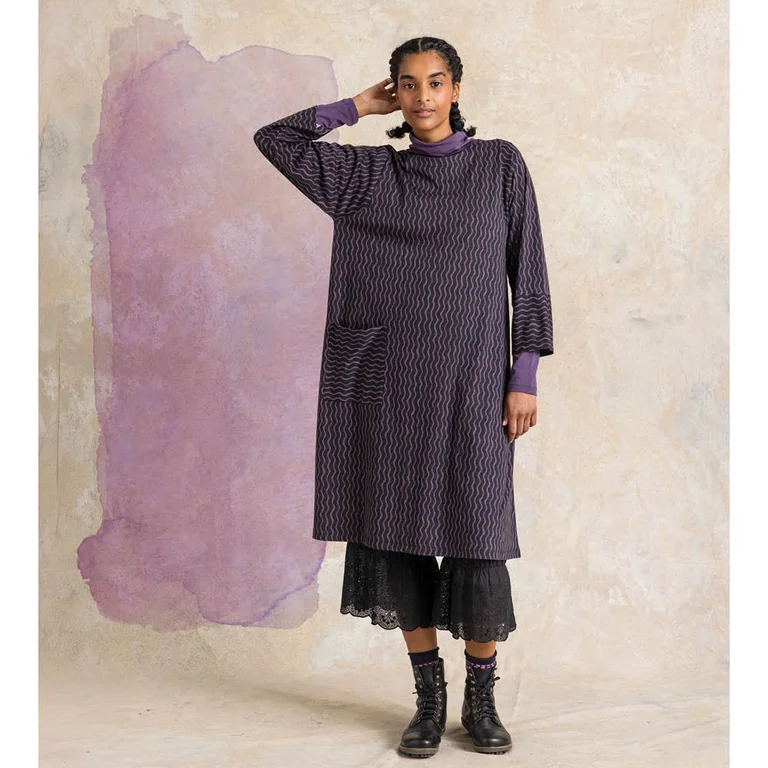 A woman wearing a dark purple patterned dress over a polo-neck jumper from Gudrun Sjödén.