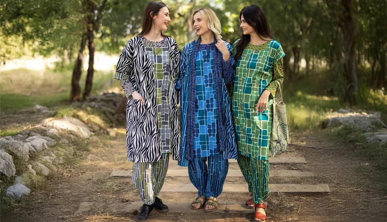 Trois femmes se tenant à l'extérieur, les unes près des autres, et portant des vêtements à motifs signés Gudrun Sjödén.