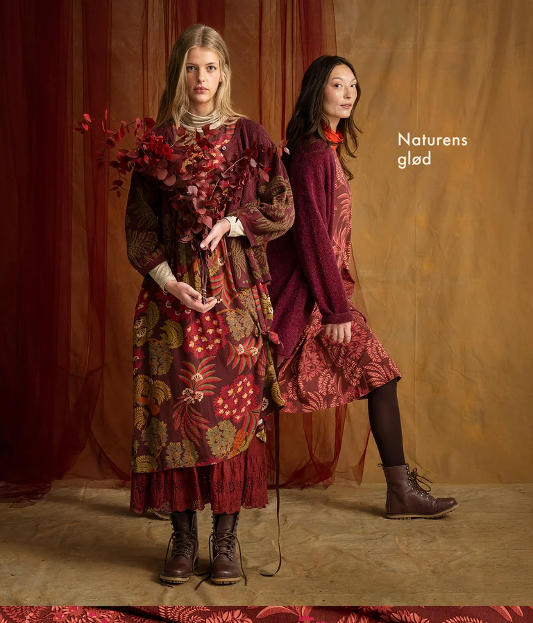Two women next to each other wearing layers of clothing in shades of red from Gudrun Sjödén.
