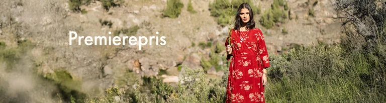 En kvinne som holder en grønn kvist foran ansiktet og er kledd i en rød omslagskjole fra Gudrun Sjödén. 