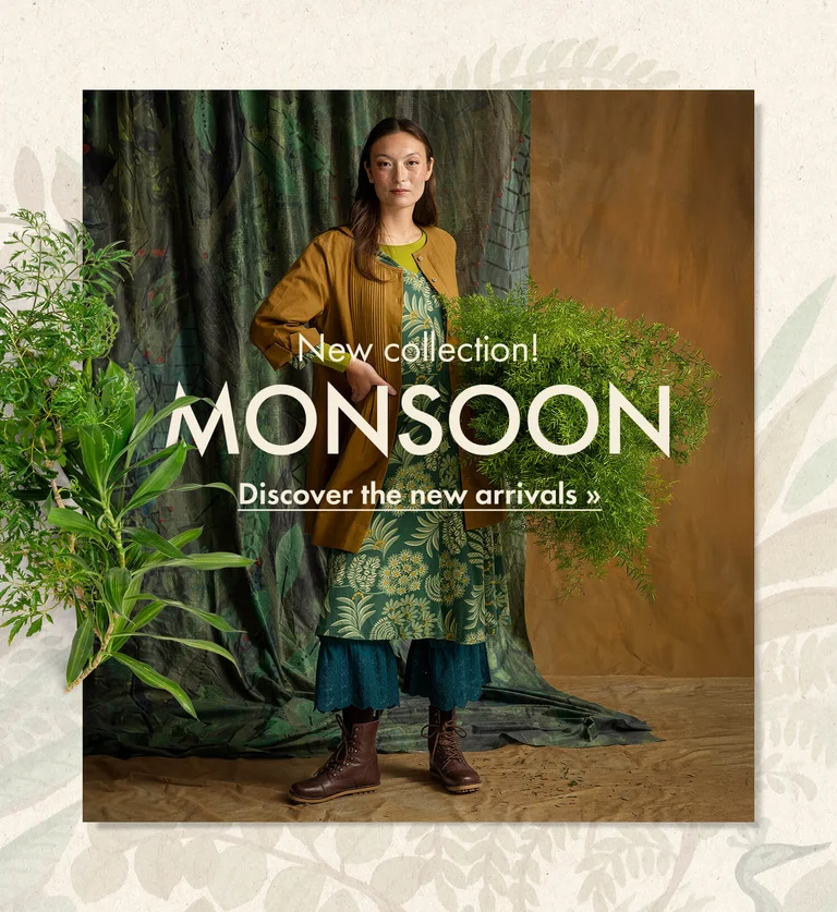 A woman with her hands in the air wearing a knitted cardigan in shades of blue from Gudrun Sjödén. The picture is framed by a botanical pattern and standout green plants.