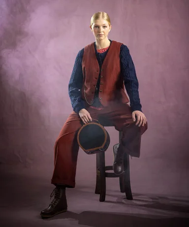 A woman sitting on a chair holding a small suitcase wearing layers of clothes from Gudrun Sjödén.