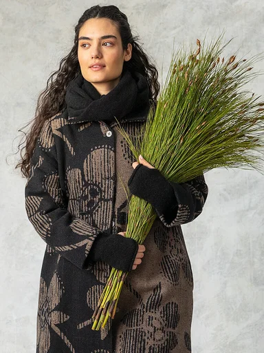 A woman wearing a patterned coat, black scarf and fingerless gloves from Gudrun Sjödén. 