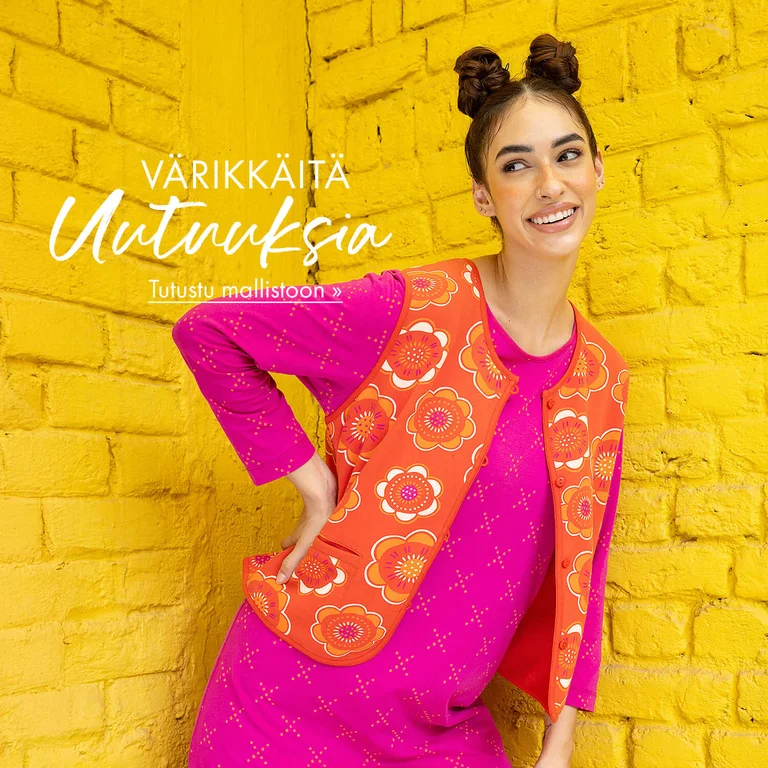 Kaksi naista poseeraa keltaista tiiliseinää vasten pukeutuneina Gudrun Sjödénin värikkäisiin vaatteisiin.