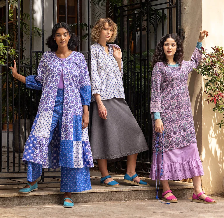 Three women in front of a large gate wearing purple and blue floral clothes from Gudrun Sjödén.