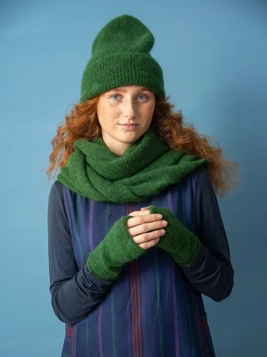 A woman wearing a green beanie, scarf and fingerless gloves from Gudrun Sjödén. 