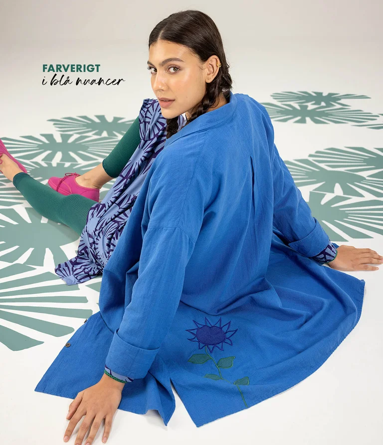 A seated woman wearing clothing in blue from Gudrun Sjödén. 