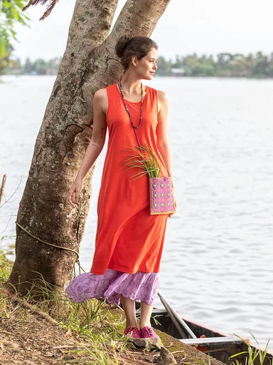 A woman wearing a pink, patterned dress and a small, pink bag adorned with mirrors from Gudrun Sjödén.