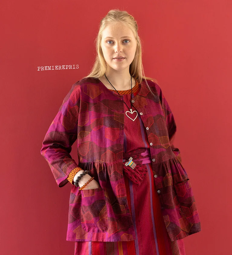 A woman wearing a red, patterned blouse and a silver heart-shaped necklace from Gudrun Sjödén’s 2025 Christmas collection. 