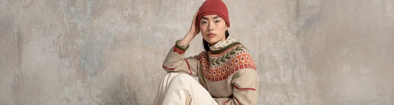 Une femme portant un pull en maille à motifs et un bonnet rouge se tient devant un fond neutre avec le texte « CLUB » en rouge.