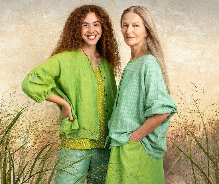 Two women standing beside one another in layers of green and turquoise clothing.  