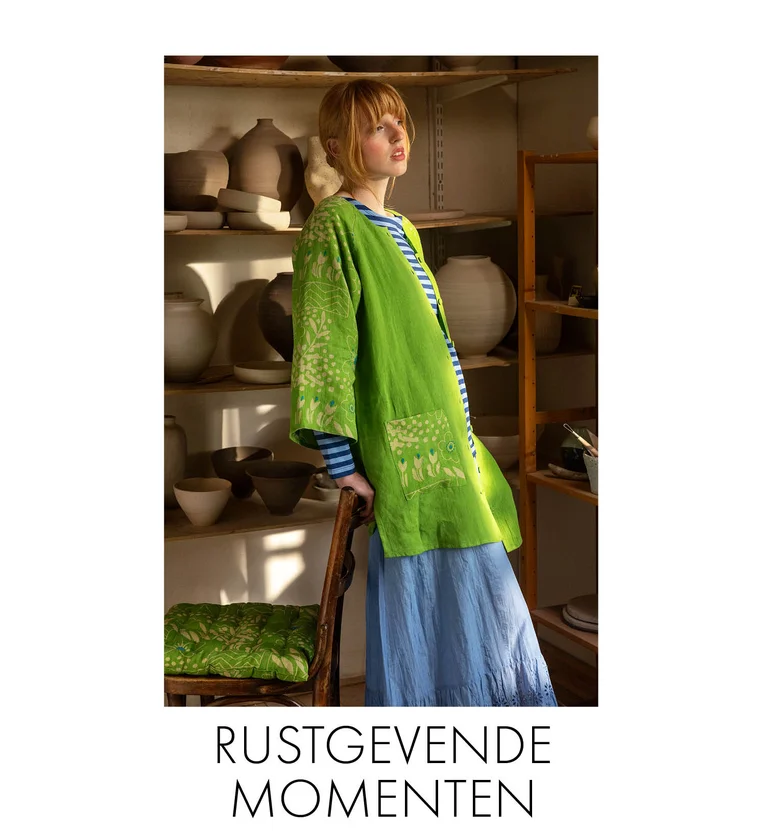 A woman in a pottery studio wearing a green “Nemorosa” linen tunic, a striped top and a light-blue skirt from Gudrun Sjödén.