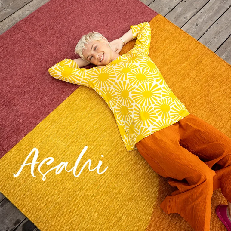Une femme allongée sur un grand tapis rouge et orange signé Gudrun Sjödén.