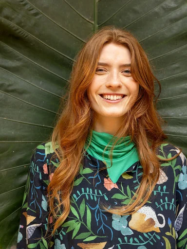 A woman wearing a green polo-neck top and patterned dress from Gudrun Sjödén.