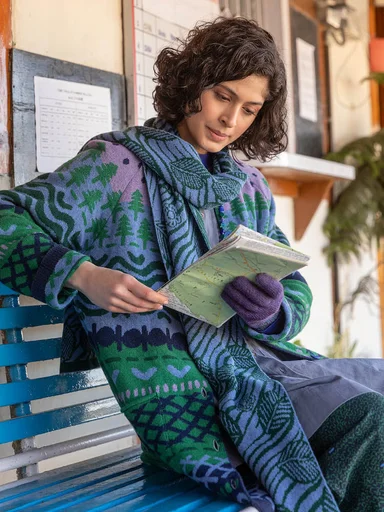A woman sitting on a bench wearing layers of clothing from Gudrun Sjödén and reading a map.