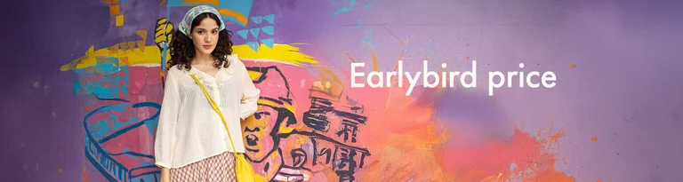 A woman standing by a wall wearing a ruffled blouse from Gudrun Sjödén. 