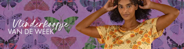 Een vrouw in een gele jurk met print staat voor een paarse muur met vlinders.
