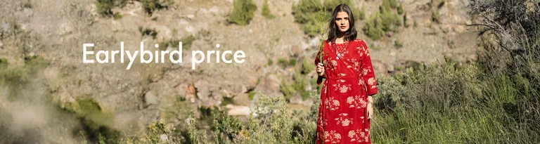 A woman holding a green branch in front of her face and wearing a red wrap dress from Gudrun Sjödén. 