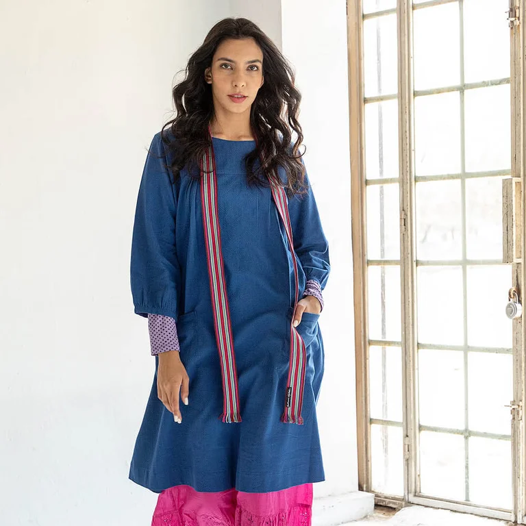Une femme portant une robe bleue tissée et un jupon rose signés Gudrun Sjödén.